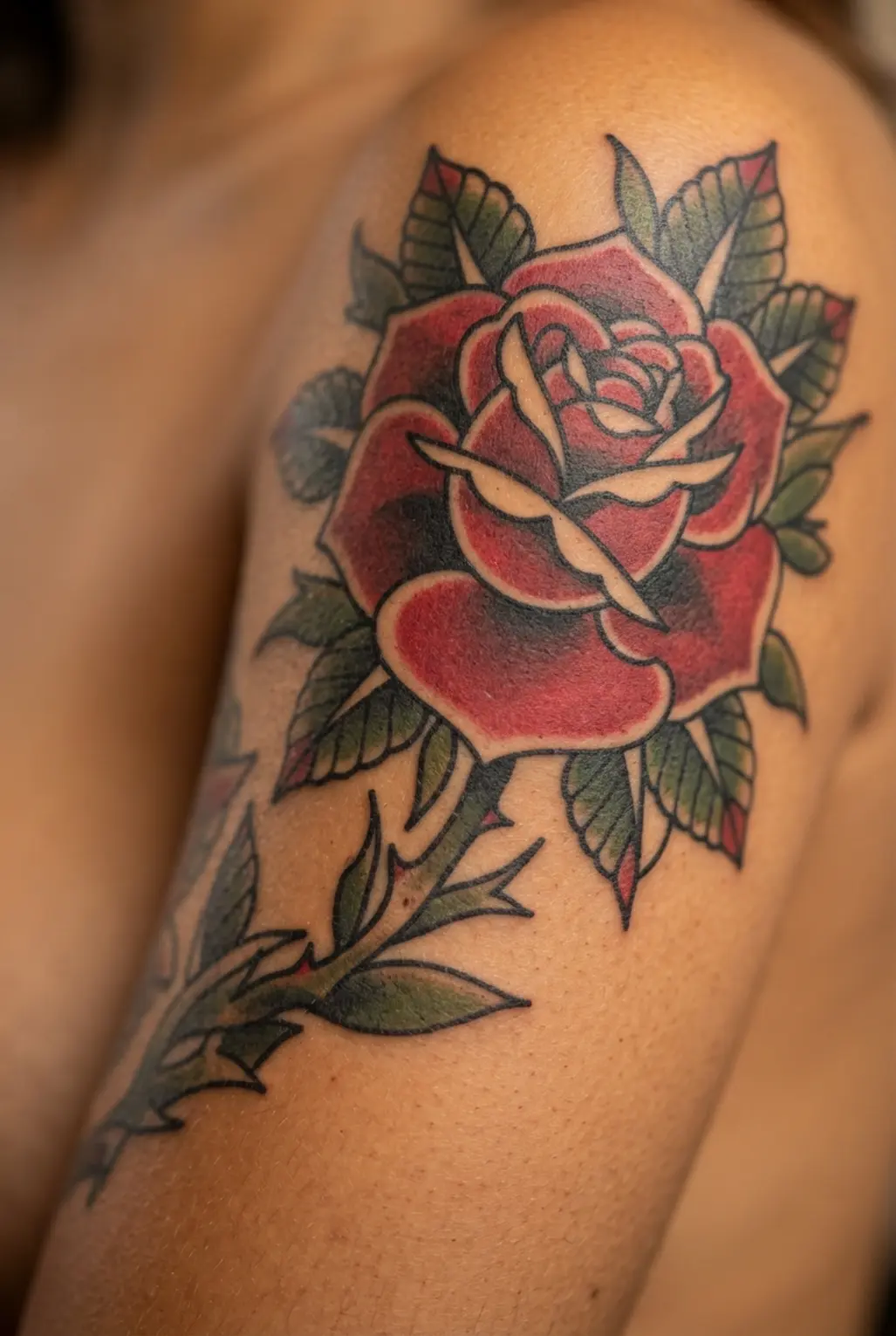 A classic traditional rose tattoo with bold lines and red shading, placed on the upper arm for a quarter sleeve design.
