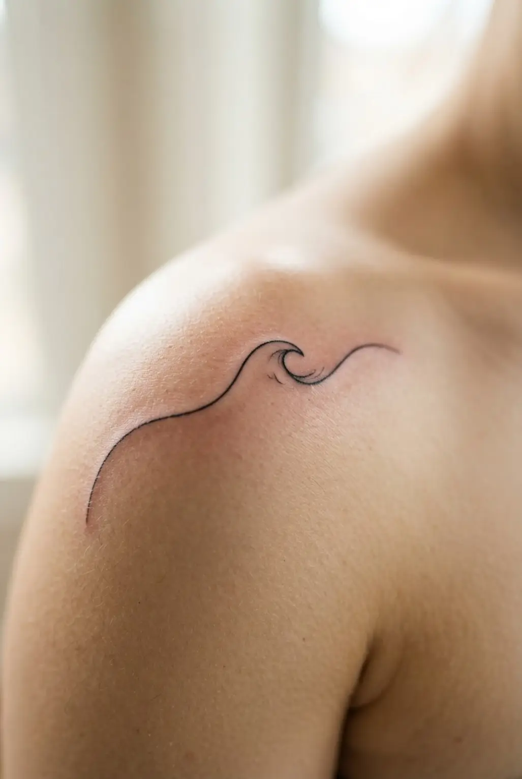 A minimalist tattoo of a single wave in fine linework, elegantly placed on the shoulder for a quarter sleeve.