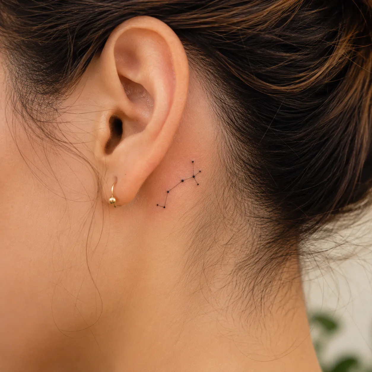 A minuscule, single-needle tattoo depicting the Sagittarius constellation behind the ear.