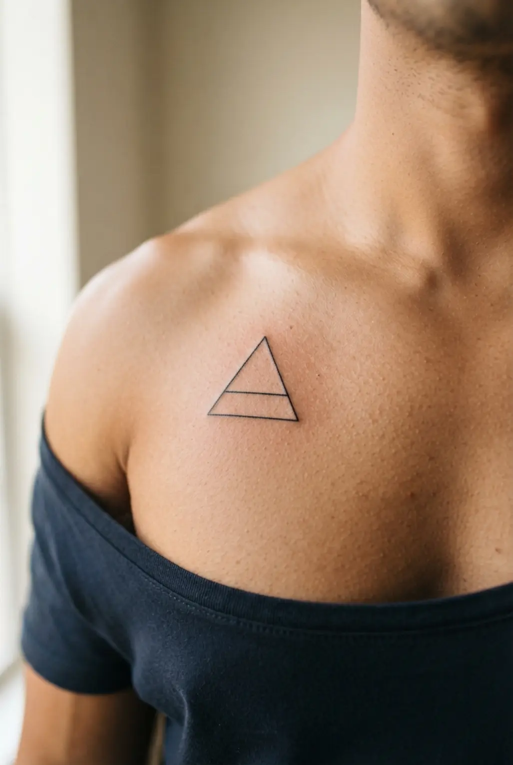 A small chest tattoo for men showing a fine-line geometric triangle in clean black ink.