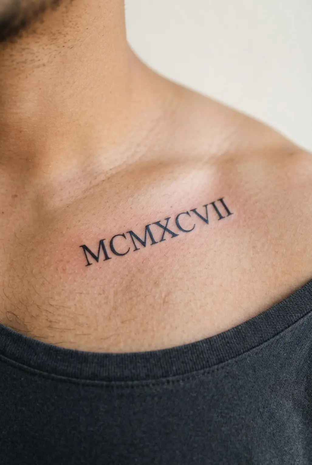 A small chest tattoo for men showing Roman numerals in refined script with fine black lettering.