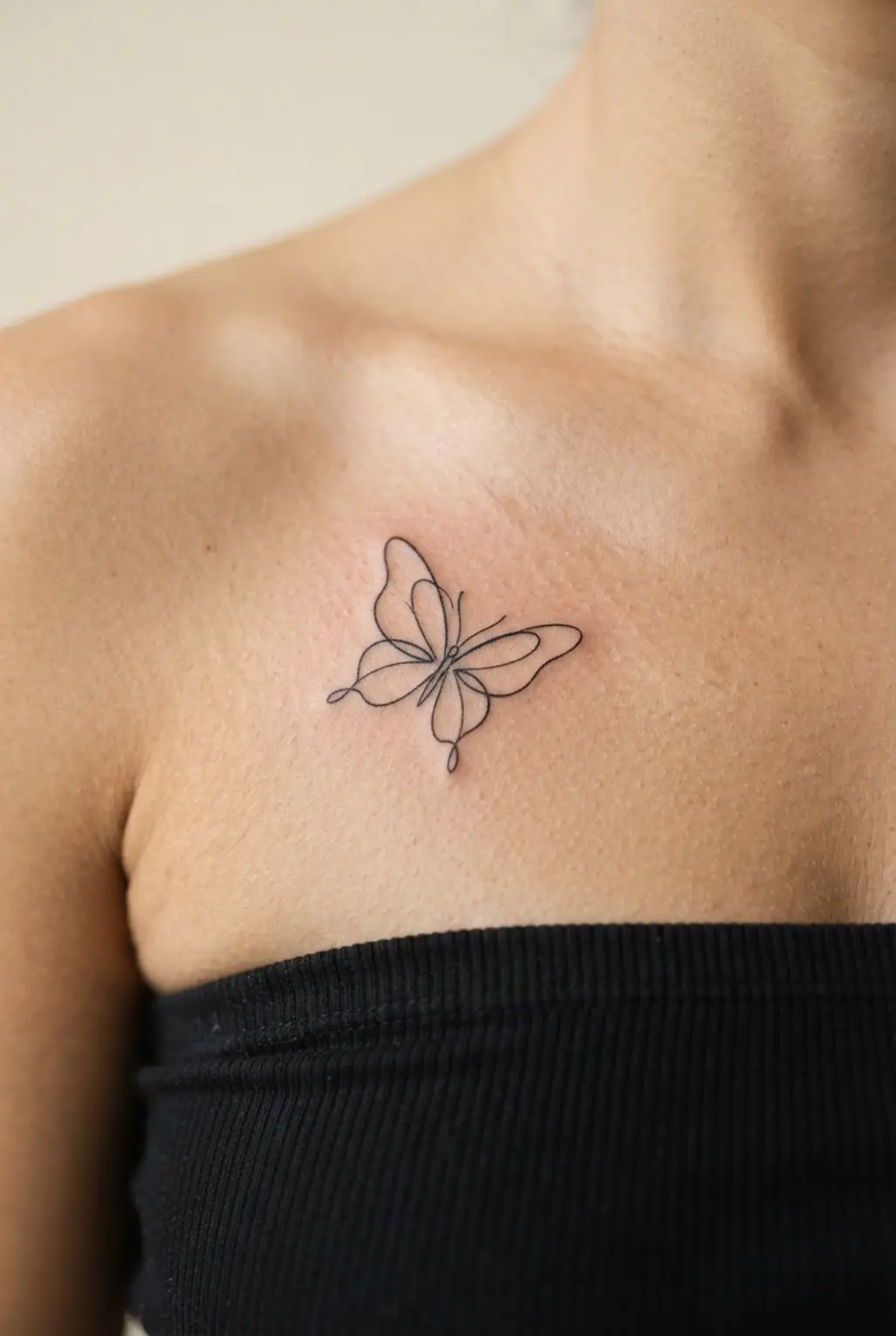 Small chest tattoos for women shown as a single-line butterfly below the collarbone.