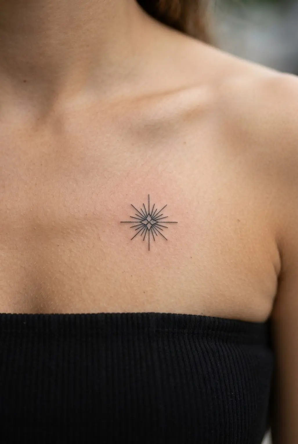 Small chest tattoos for women shown as a geometric sun star in fine black linework.
