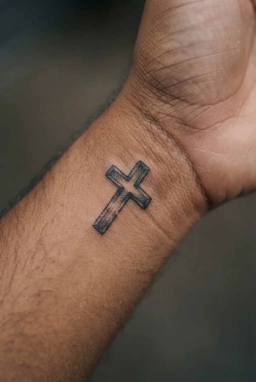 Short wooden cross with etched grain lines on a man's wrist, styled as a small cross tattoo for men.