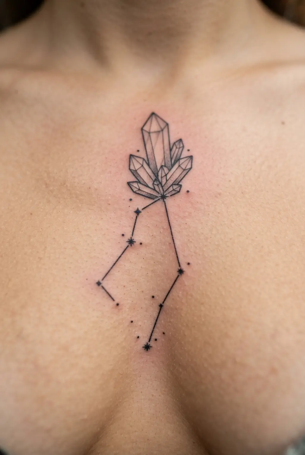 A centered sternum tattoo pairing a linear Virgo constellation with a clear quartz crystal design.