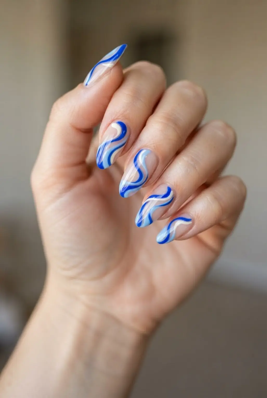 Electric light blue abstract swirl nails with curving cobalt lines and pale accents.